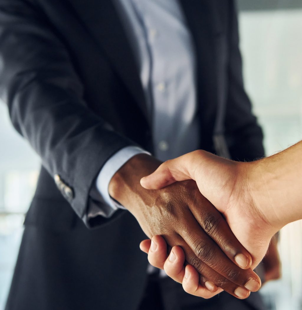 Doing handshake with customer. Young african american businessman in black suit is indoors